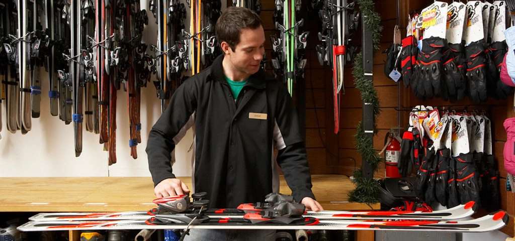 Une personne employée d’un centre de location d’équipement sportif hivernal ajuste des fixations sur une paire de skis.