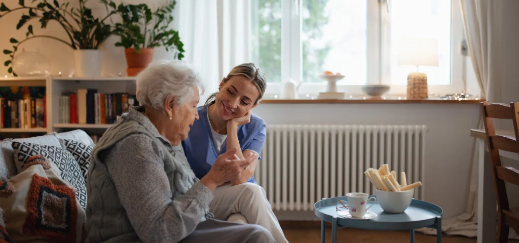A healthcare worker visiting a senior at home, having a conversation in the living room.