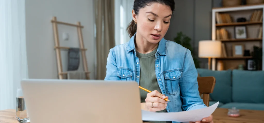 Une jeune femme consulte son ordinateur et prend des notes.