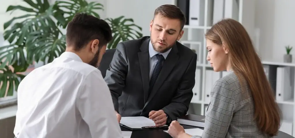 Un homme et une femme sont assis face à un professionnel, qui leur présente des documents dans un bureau.