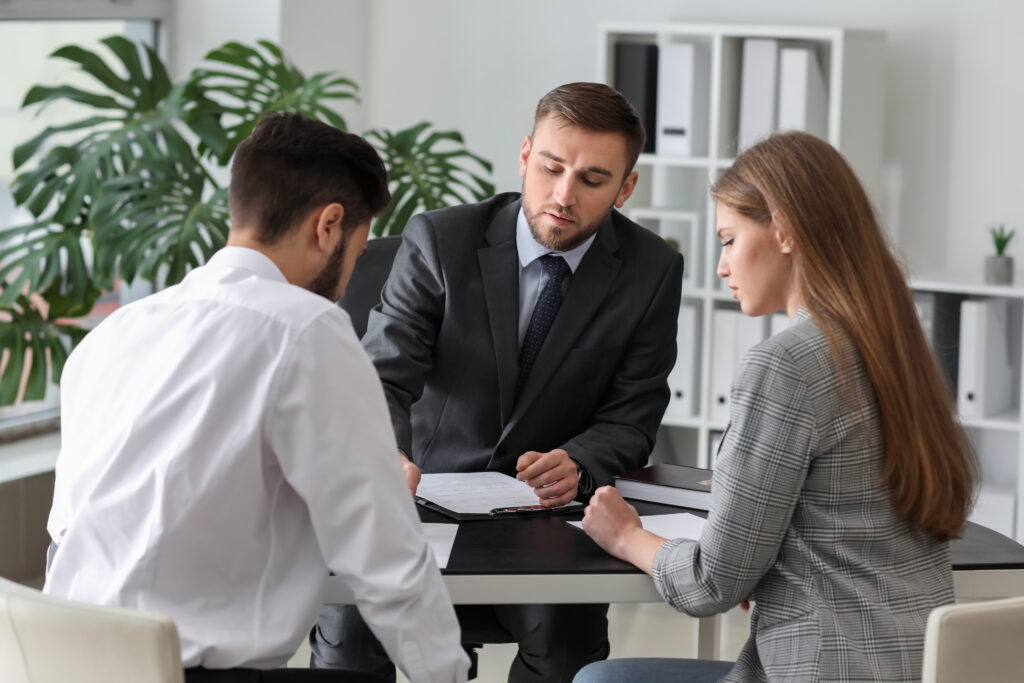 Un homme et une femme sont assis face à un professionnel, qui leur présente des documents dans un bureau.