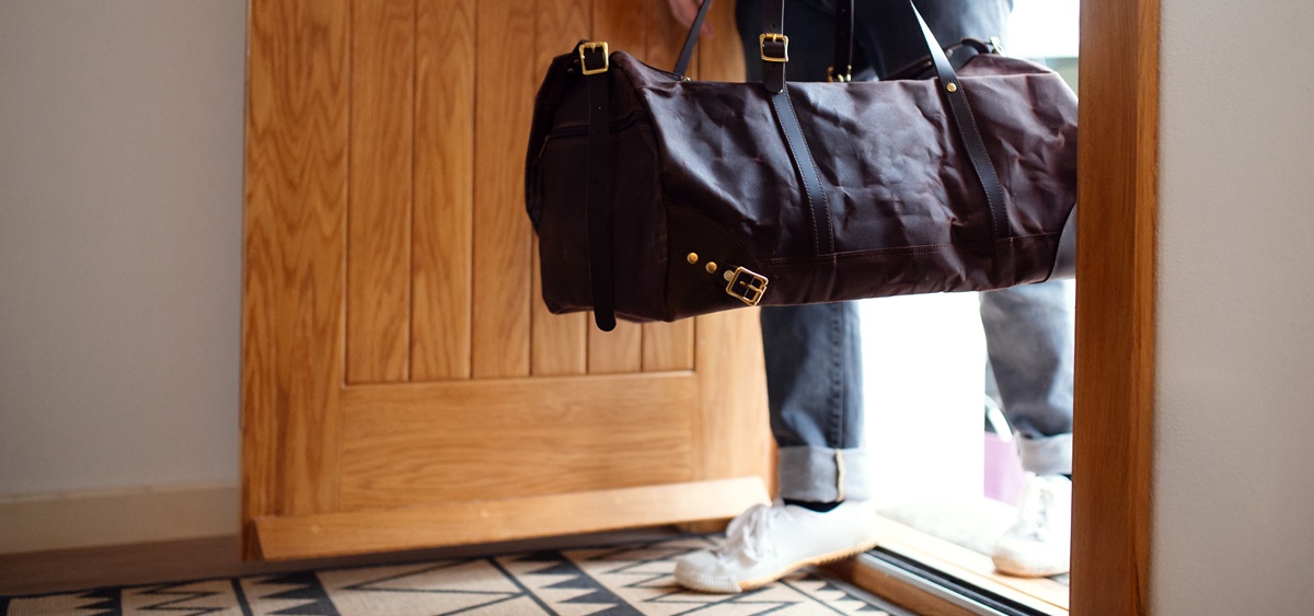 A man opens the door of his home with a bag in hand. 