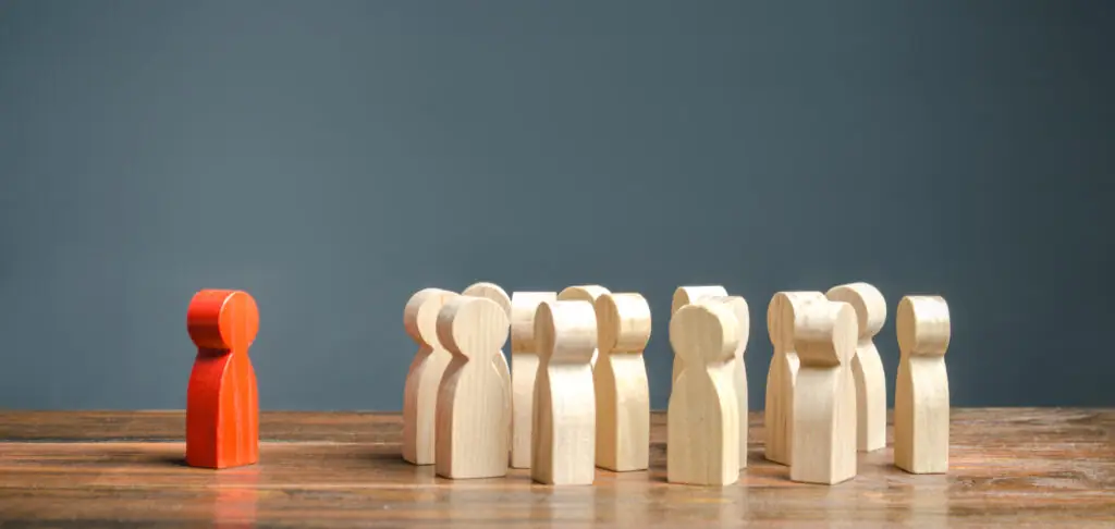Discrimination et isolement Une figurine en bois teinte en rouge se tient à l’écart de la foule constituée d’autres figurines de couleur beige.