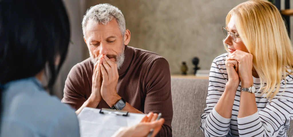 Un homme et une femme sont assis sur le canapé de leur maison avec un conseiller financier.