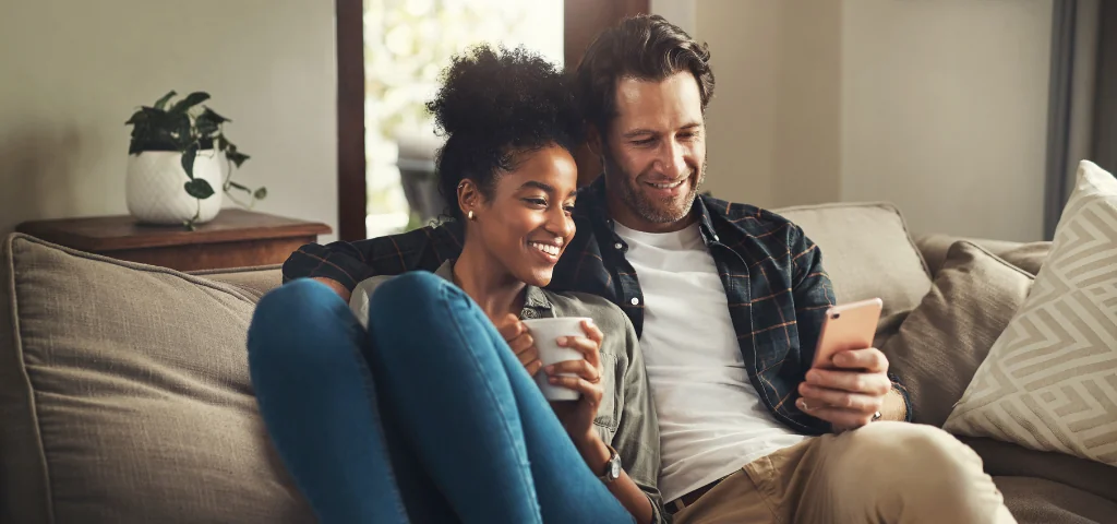 A couple on a couch smiling while looking at a cell phone screen  