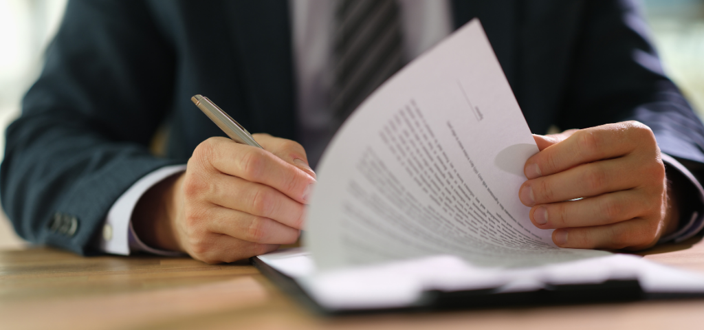 A man, of whom only the torso and hands are visible, is signing a document.