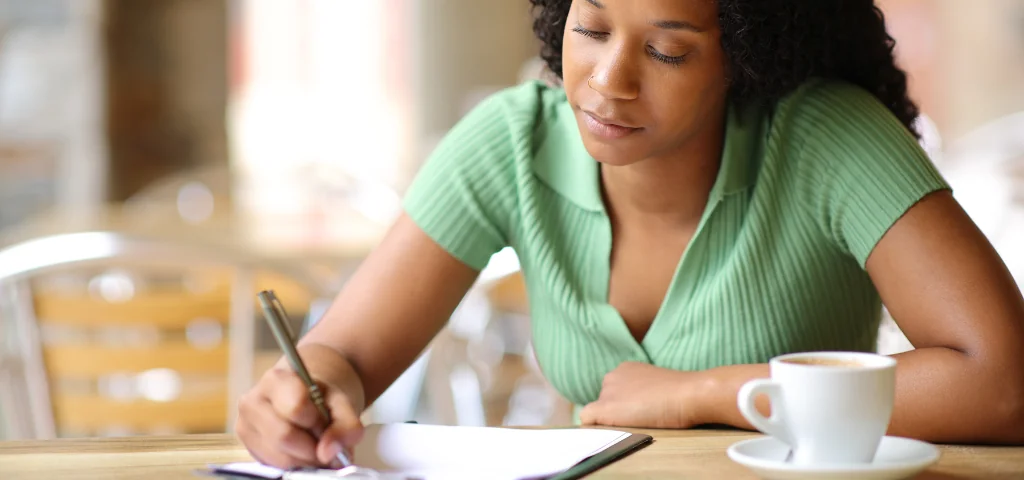 A person wearing a green sweater is sitting at a table filling out a paper form.