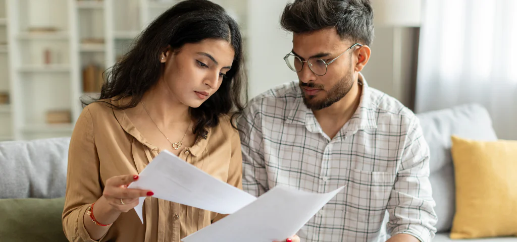 A man and a woman are sitting on a sofa, reading legal documents.