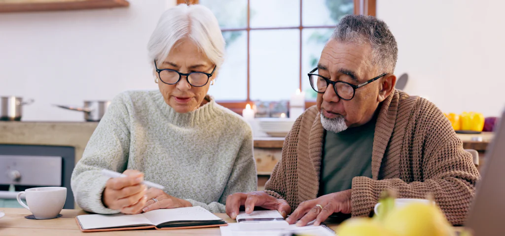 Two people are sitting in a kitchen, looking at some documents together.