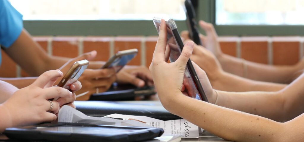 Cellphones are no longer allowed in schools. Students seated around a table using their mobile devices.