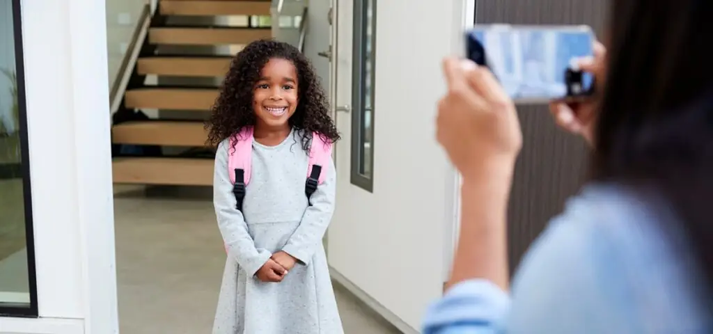Oversharenting Mother taking photo of Daughter with cell phone on first day back at school.