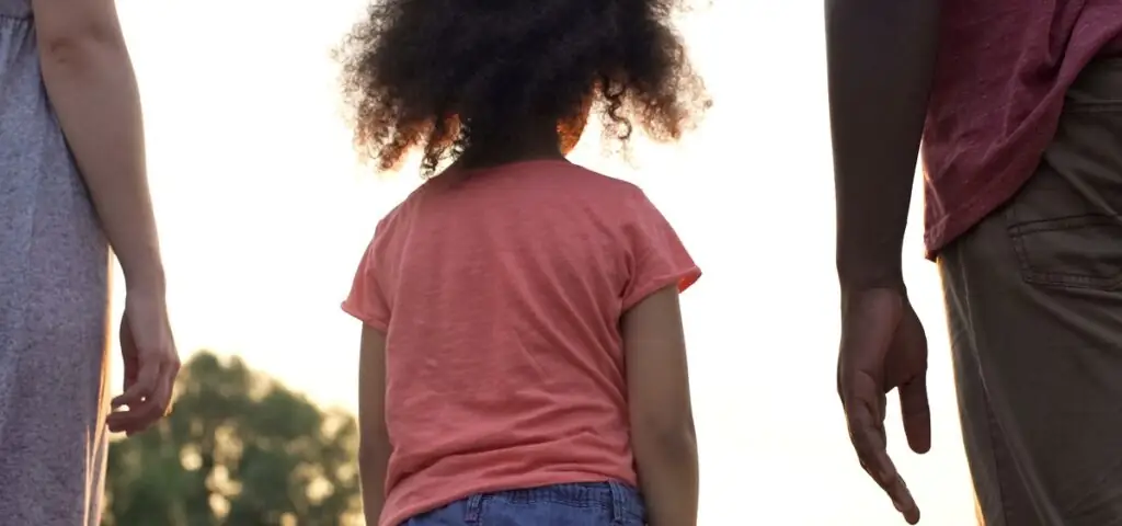 Vous pouvez demander une pension alimentaire pour vos enfants même si l’autre parent vit à l’étranger. Un enfant de dos, debout entre deux adultes.