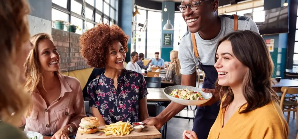 Soirée au restaurant entre amies Un serveur dans un restaurant amène un hamburger et une salade à un groupe de quatre clientes.
