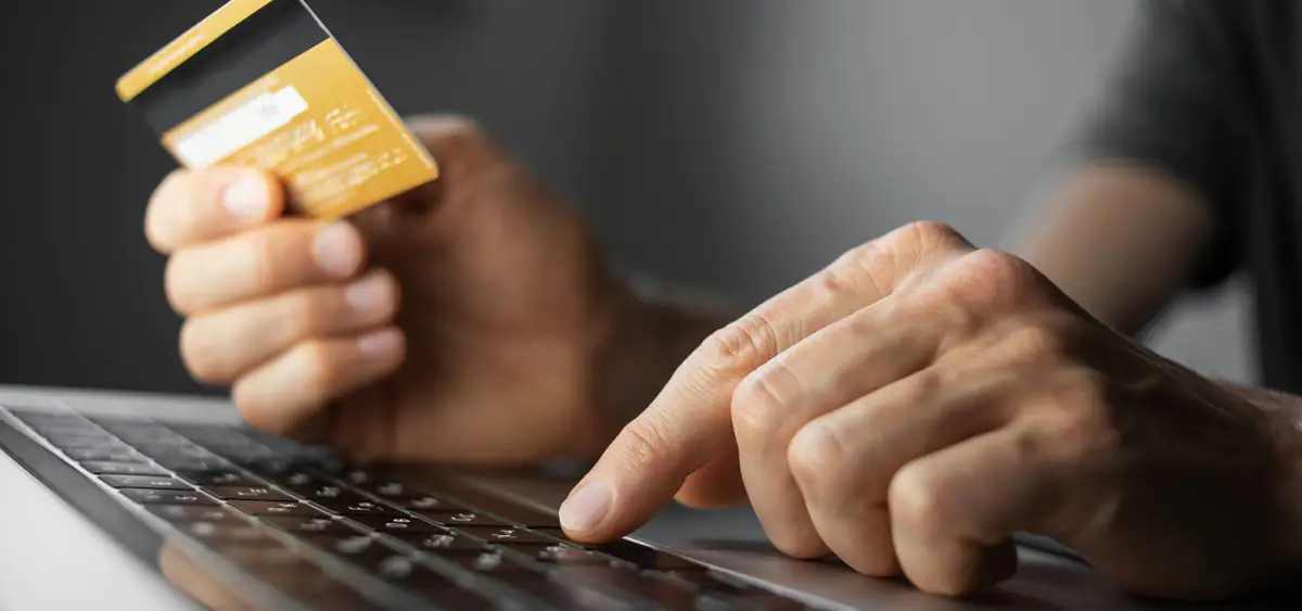 A person sitting in front of a laptop, holding a credit card in their hand.